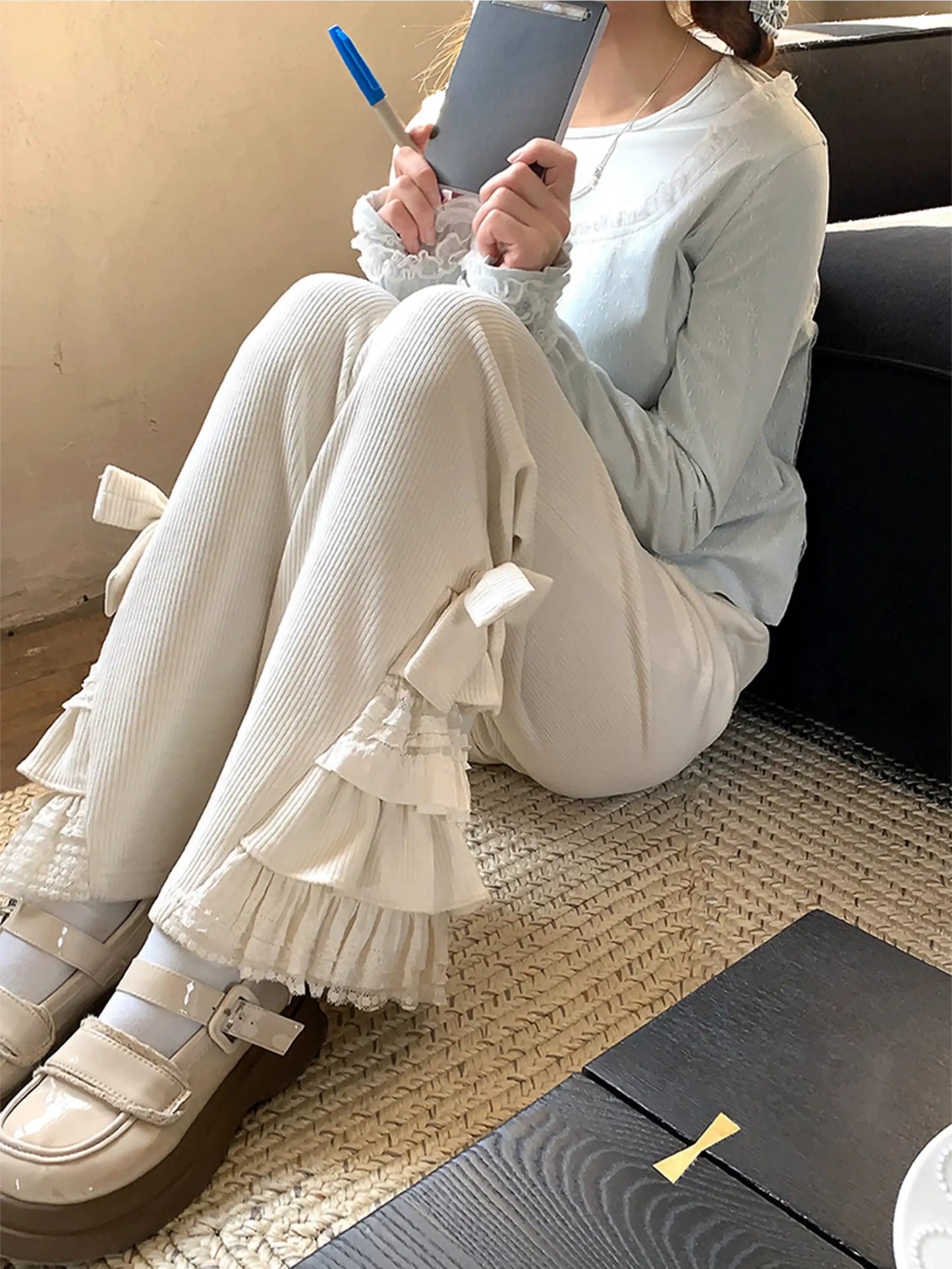 Person wearing light blue top and beige ruffled pants sitting on a couch.