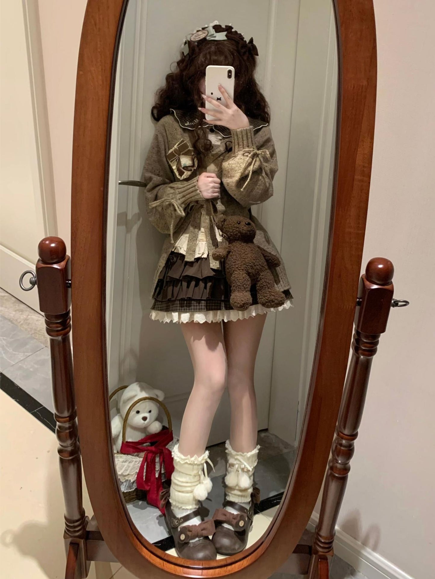 Person taking a mirror selfie wearing a detailed outfit with a teddy bear and standing in front of a wooden mirror.