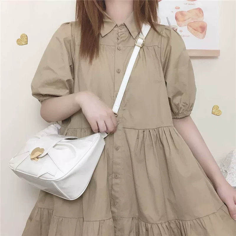 Person wearing a beige dress holding a white bag against a light-colored wall.