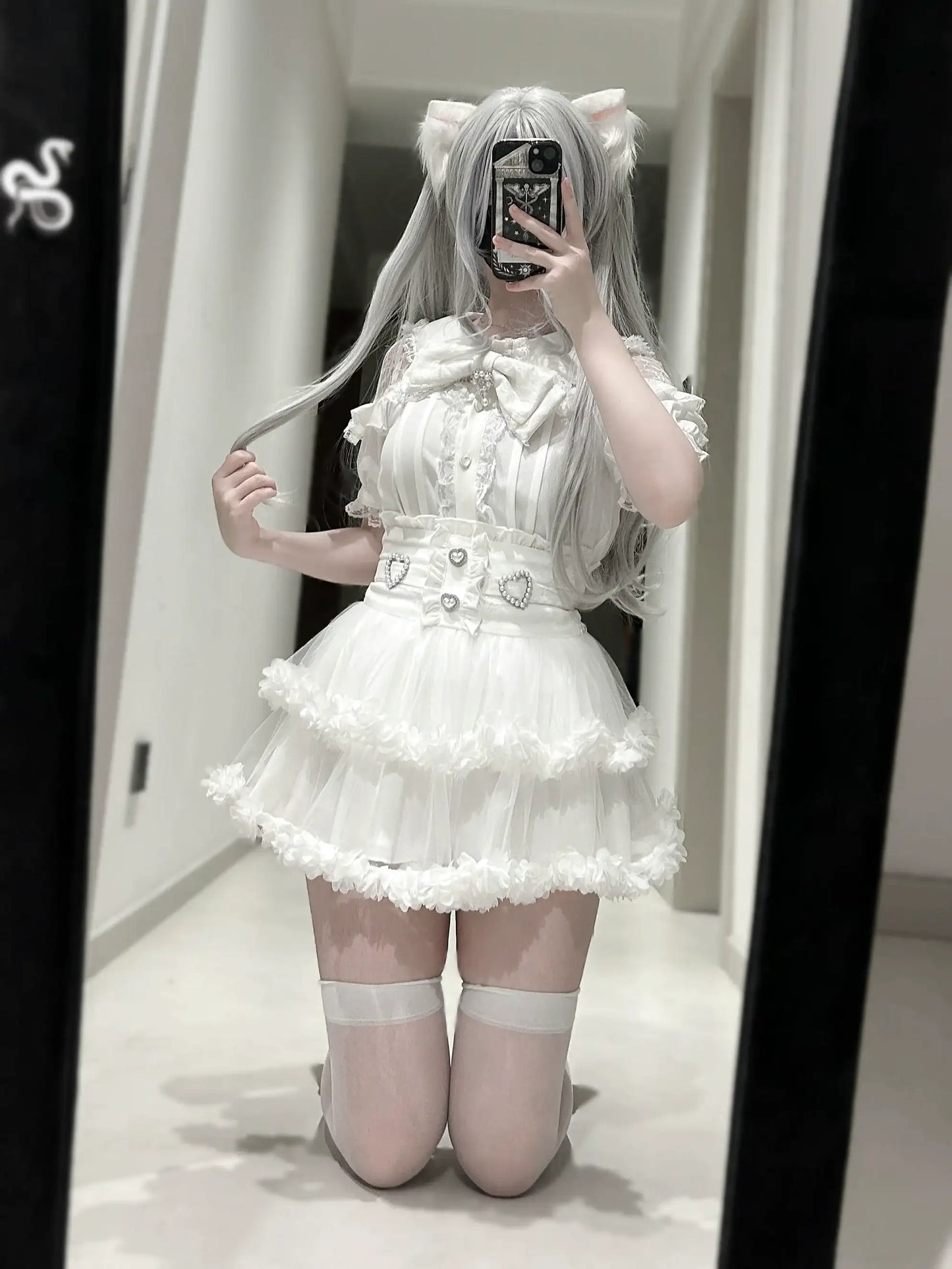Person wearing a white dress with ruffles and a belt, standing in front of a mirror.
