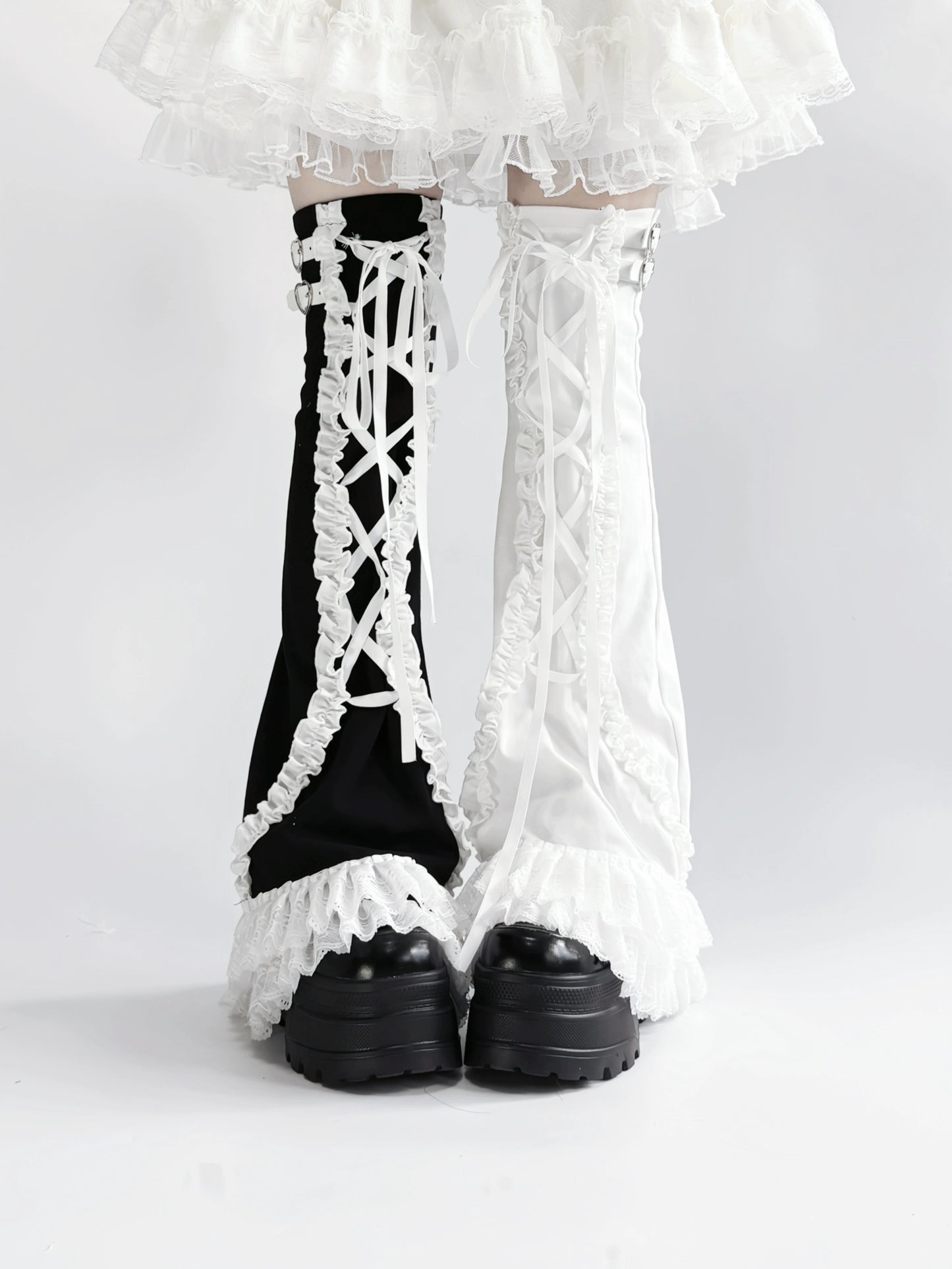 Black and white lace-up leg warmers with ruffled details on a plain background