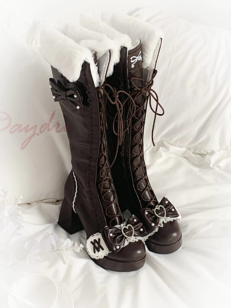 Pair of brown knee-high boots with lace details on a white background