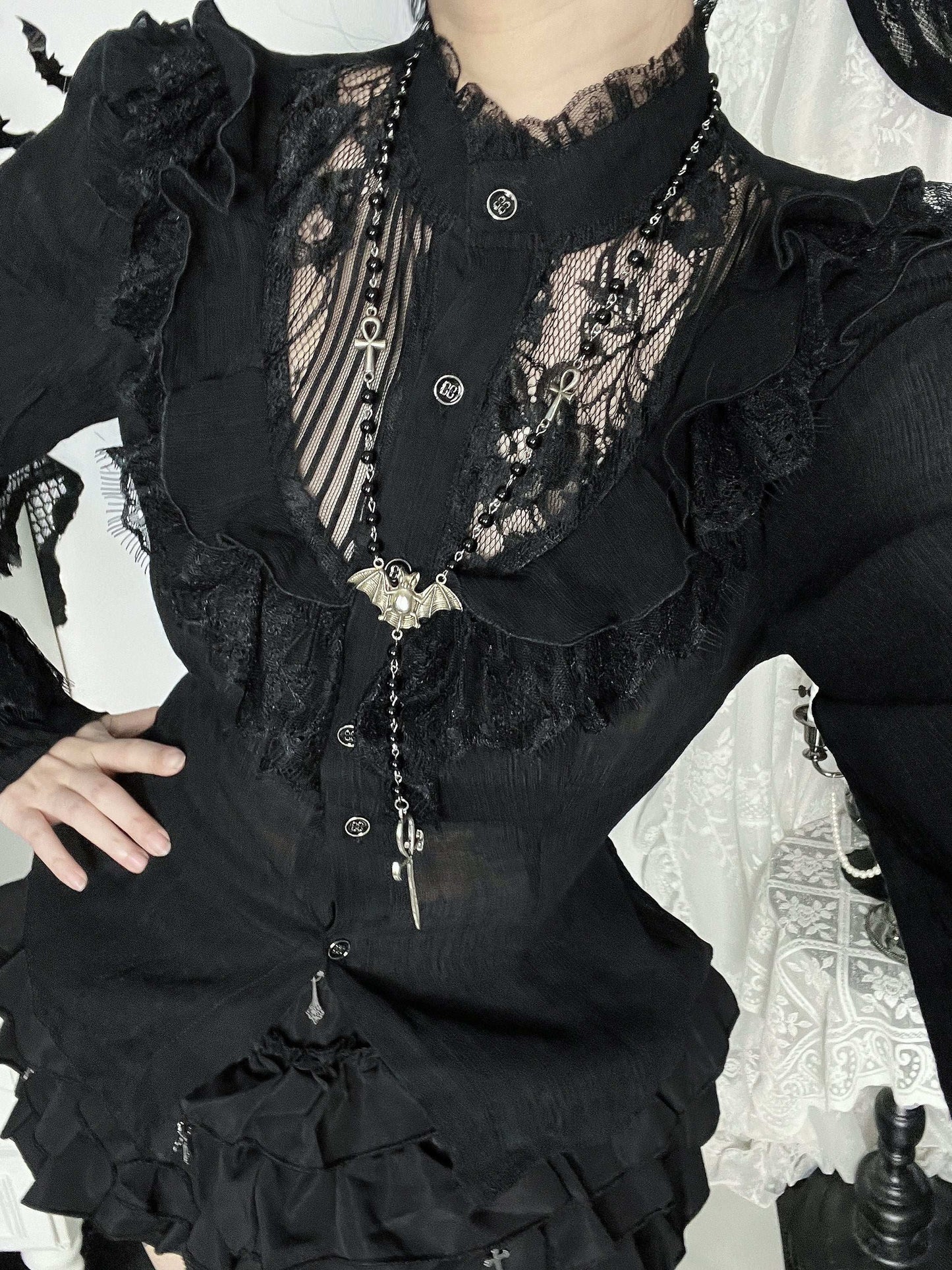 Person wearing a black lace top with ruffled details and a necklace.