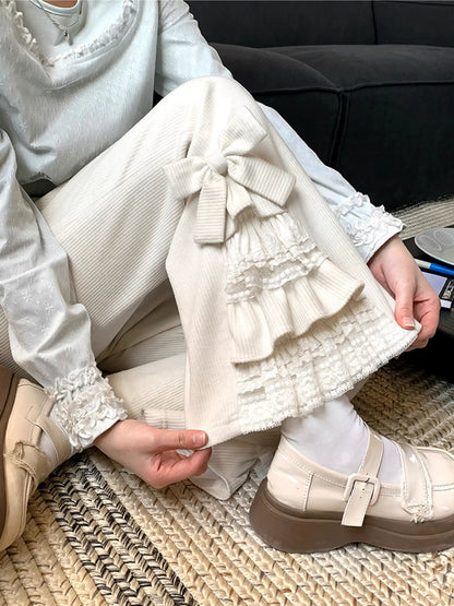Person wearing a white outfit with ruffled pants and beige shoes on a textured surface.