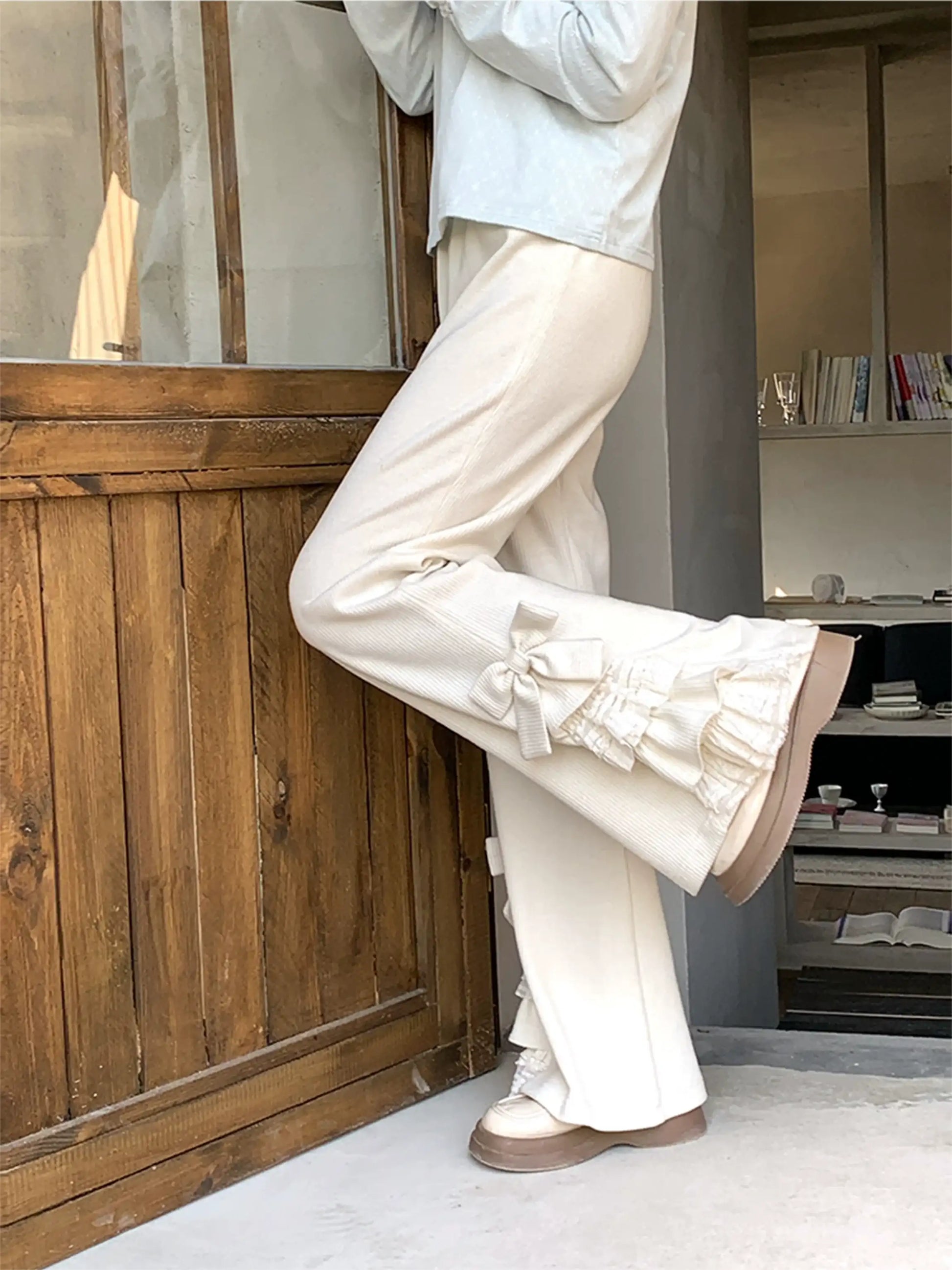 Person wearing white pants and a light blue shirt in a room with wooden paneling and shelves.