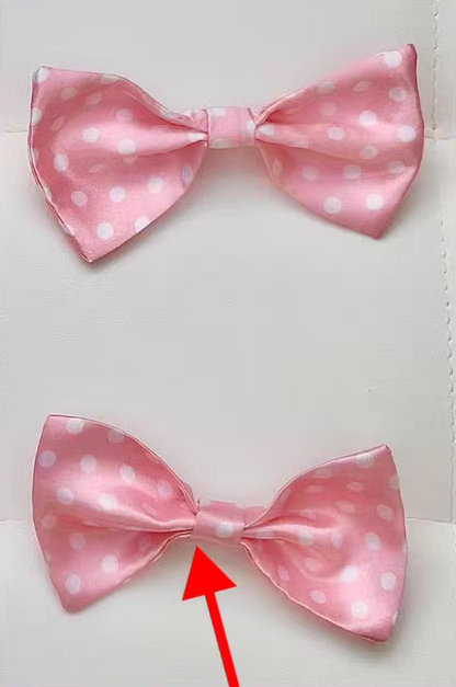 Two pink satin bow ties with white polka dots are shown on a white background, with a red arrow pointing to the center of the lower bow tie.