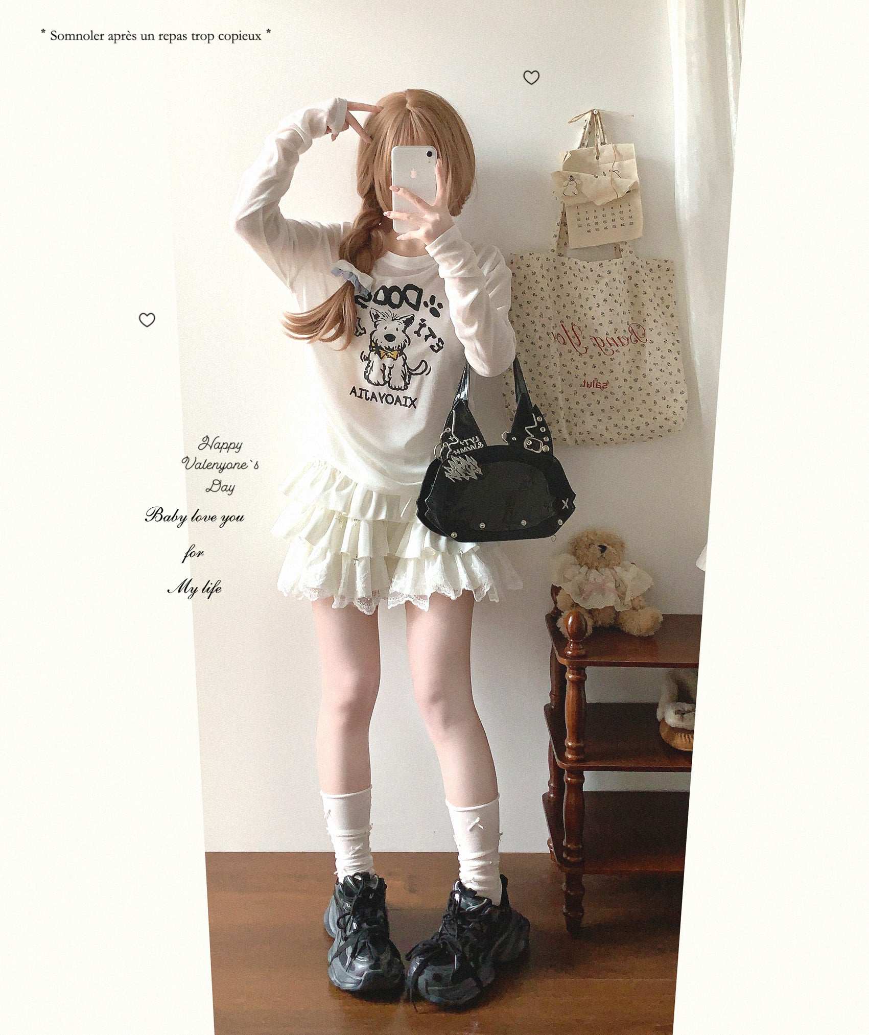 Person wearing a white outfit with a graphic design, standing in a room with a wooden shelf and teddy bear.