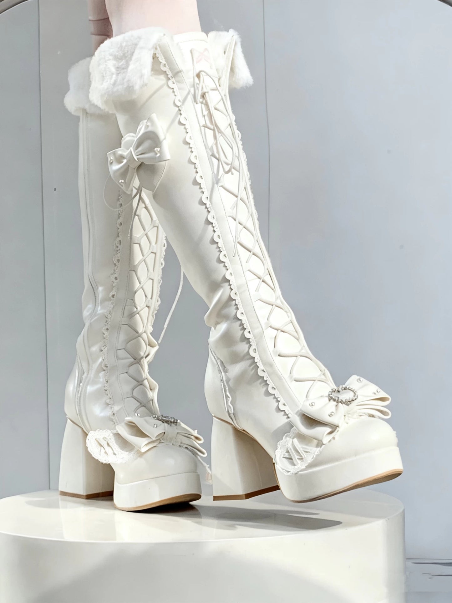 White lace-up platform boots on a white pedestal against a light gray background