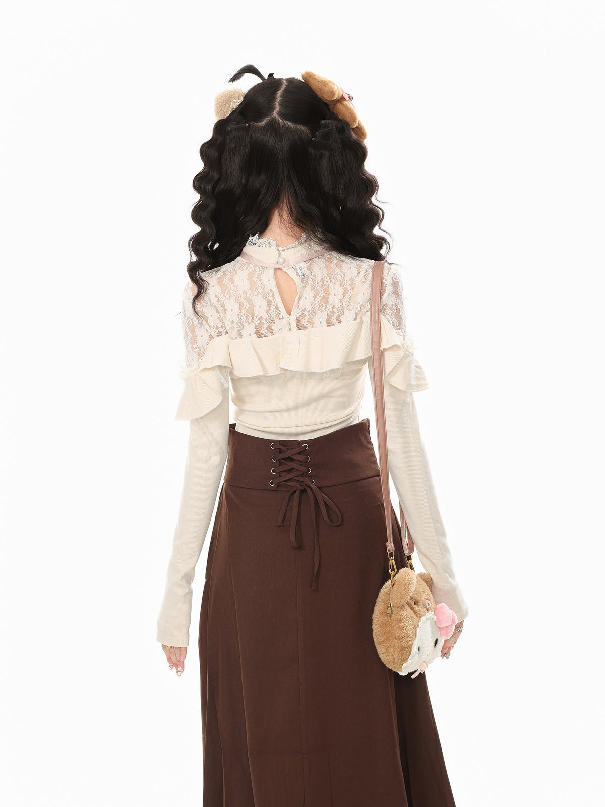 A model shown from the back wearing a cream long-sleeve top with a lace back and ruffle details, paired with a brown lace-up skirt. She is carrying a small round plush crossbody bag with a pink bow and brown plush ear accents.