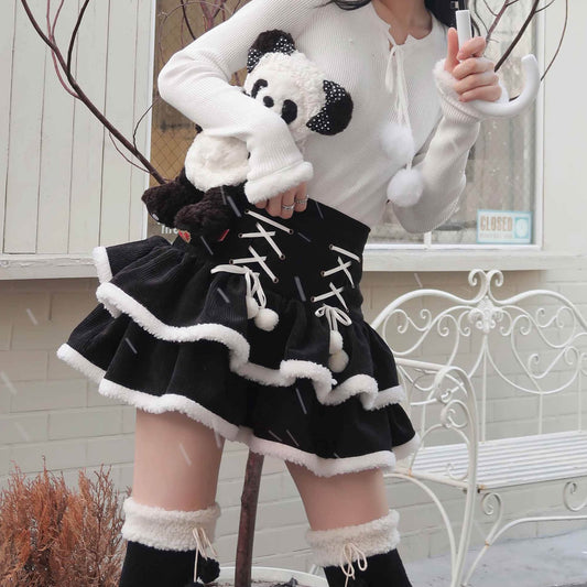 A person wearing a black and white outfit with a panda design top and a high-waisted ruffled skirt with fur edges, sitting on a white bench.