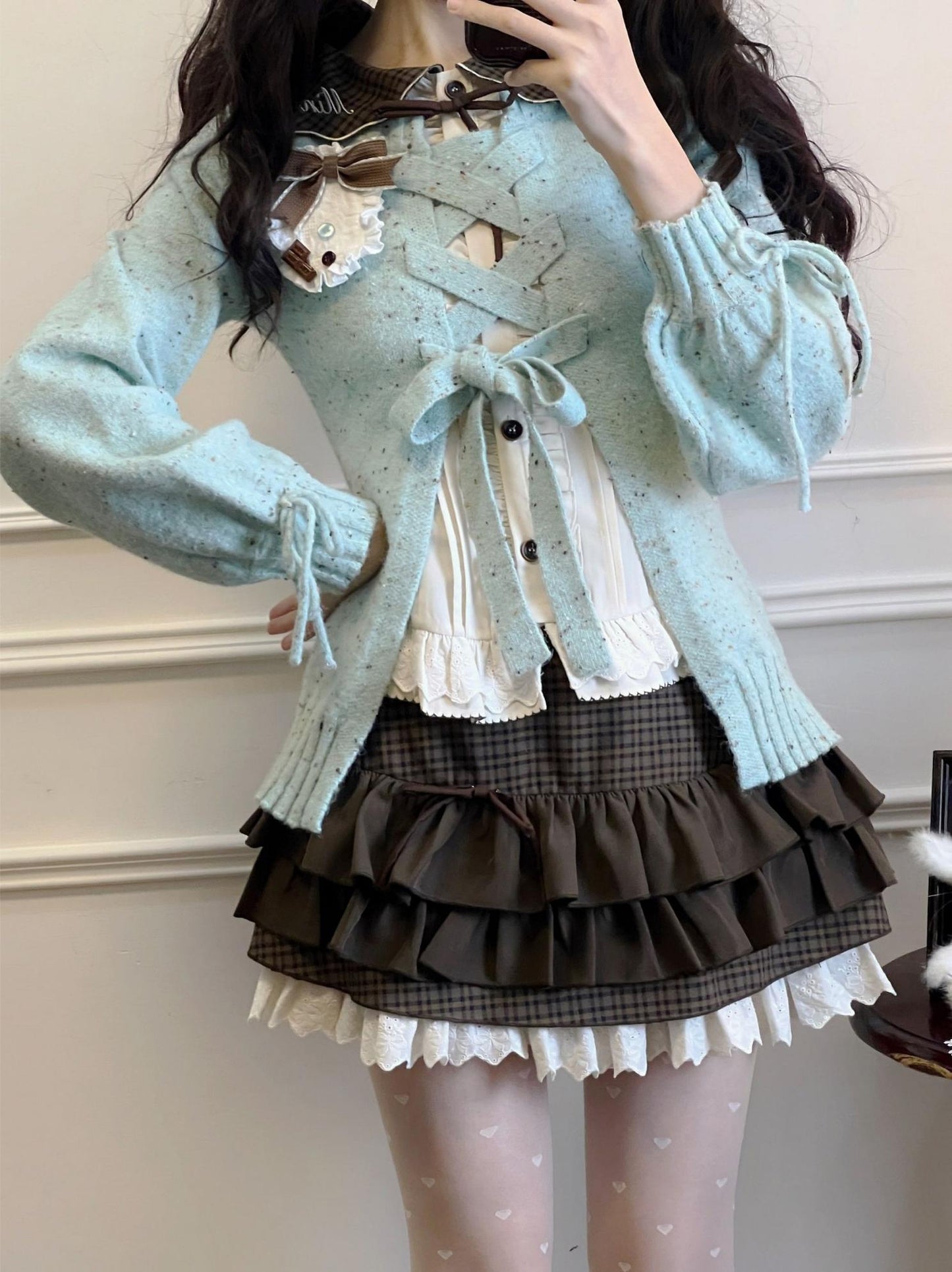 Person wearing a light blue cardigan over a plaid skirt with a white blouse.