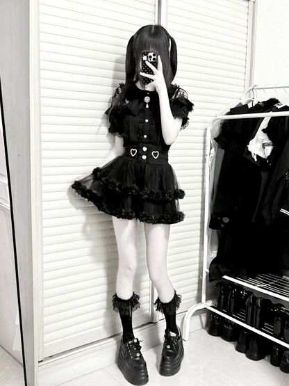 Person wearing a black outfit with heart details in a room with white walls and a rack of clothes.