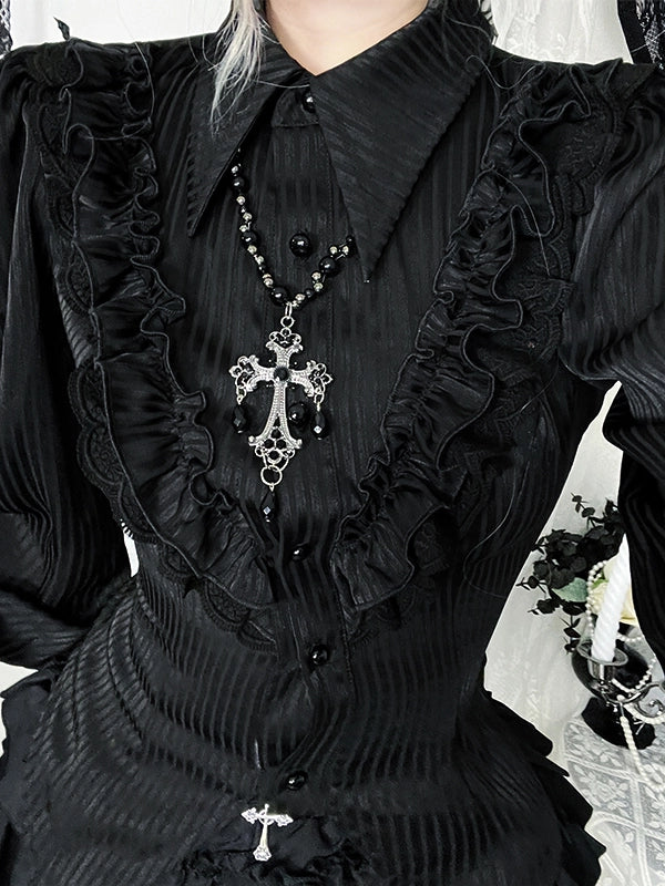 Close-up of a person wearing a black dress with ruffles and a prominent necklace with a cross pendant.