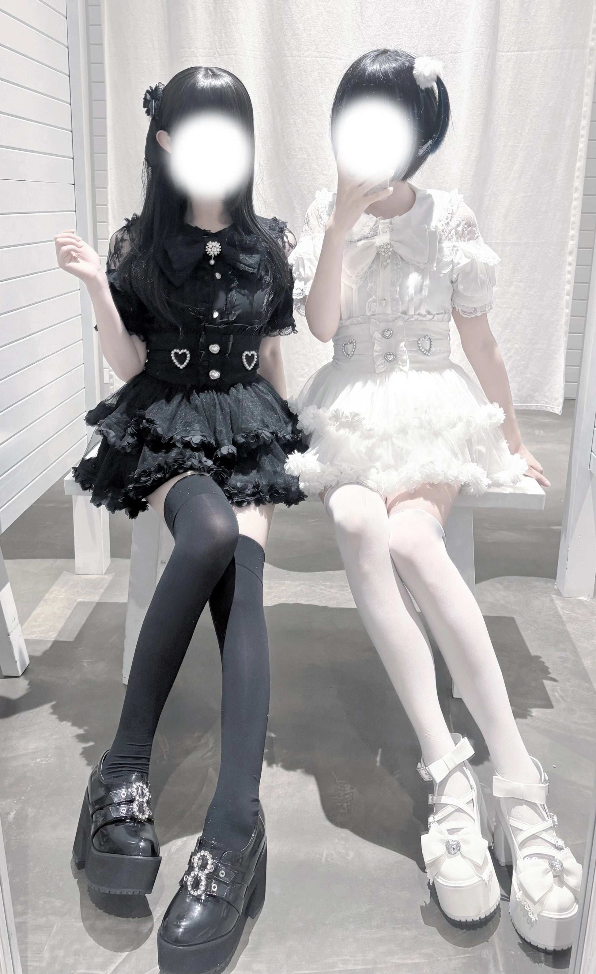 Two people wearing black and white outfits with heart details, sitting on a bench.