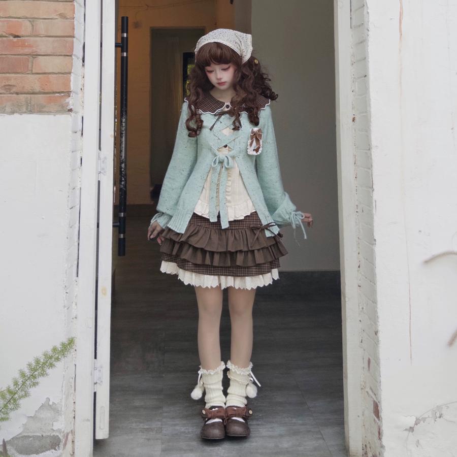 Woman in a light green cardigan and brown skirt standing in an open doorway.
