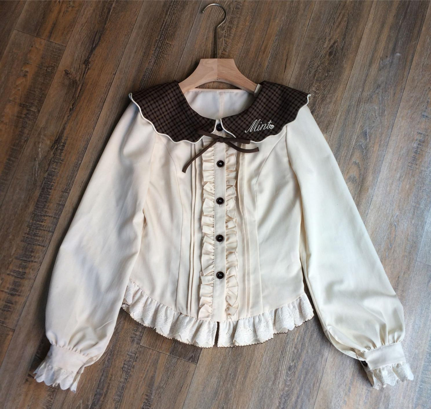 White blouse with brown collar and plastron on a wooden hanger against a wooden background