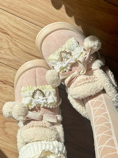 Pair of pink boots with lace details and pom-poms on a wooden floor.