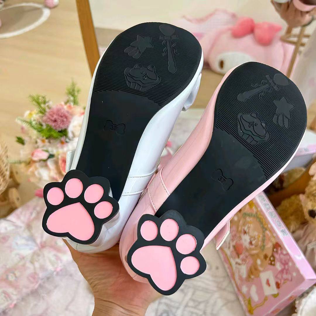 White shoes with pink paw print soles held by a hand against a blurred background