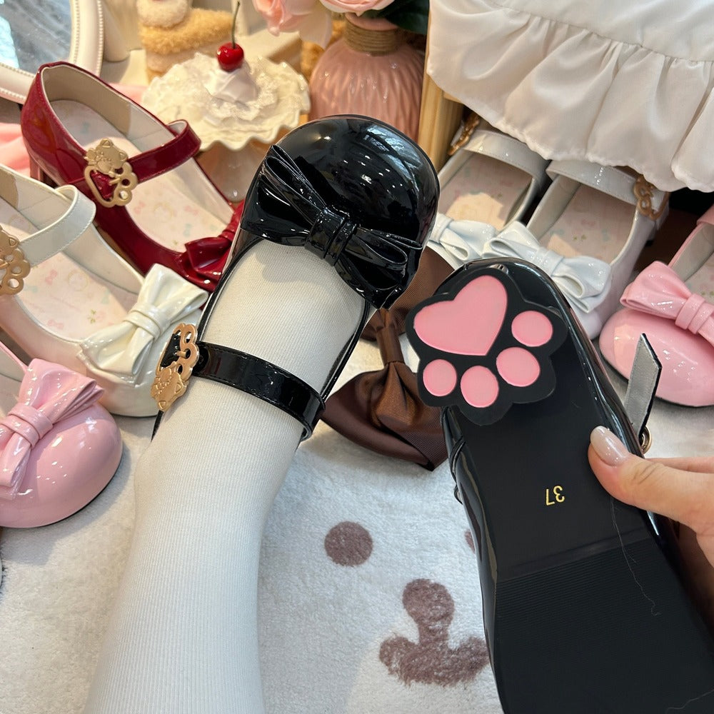 Black shoe with pink paw print design held by a hand, surrounded by children's shoes.