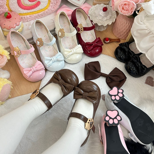 Collection of children's shoes with bows and paw prints on a soft surface.