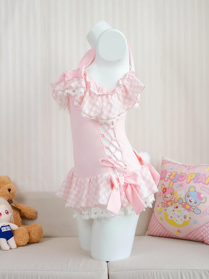 Pink ruffled swimsuit dress on a mannequin with a teddy bear and colorful pillow in the background