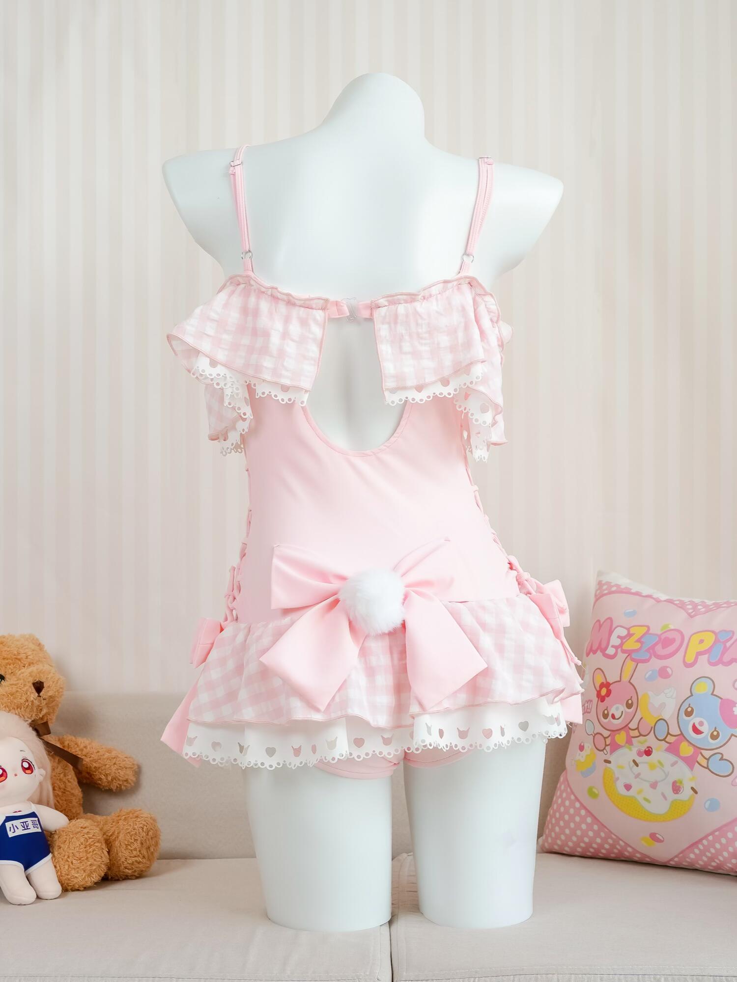 Pink swimsuit dress on a mannequin with a teddy bear and pillow in the background