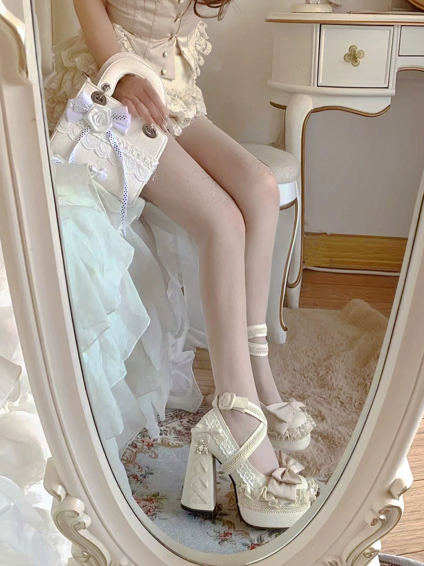 Person wearing white lace shoes and stockings sitting on a chair in front of a mirror.
