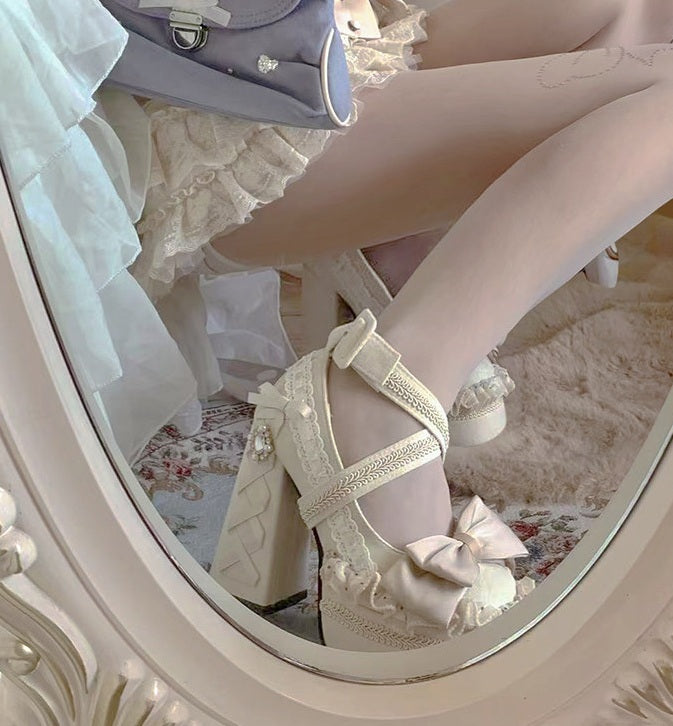 Close-up of a person wearing white lace high heels with a decorative bow, sitting on a floral-patterned chair.