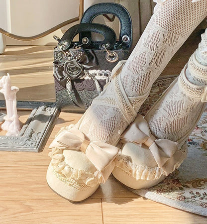 Beige lace-up shoes with decorative bows on a wooden floor.