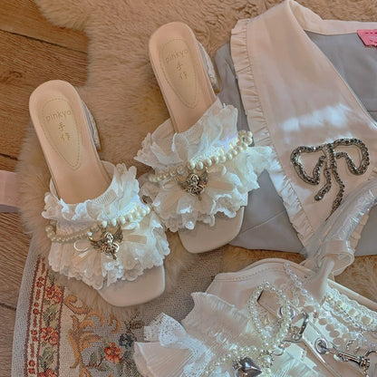 White sandals with lace and pearl embellishments on a textured surface.