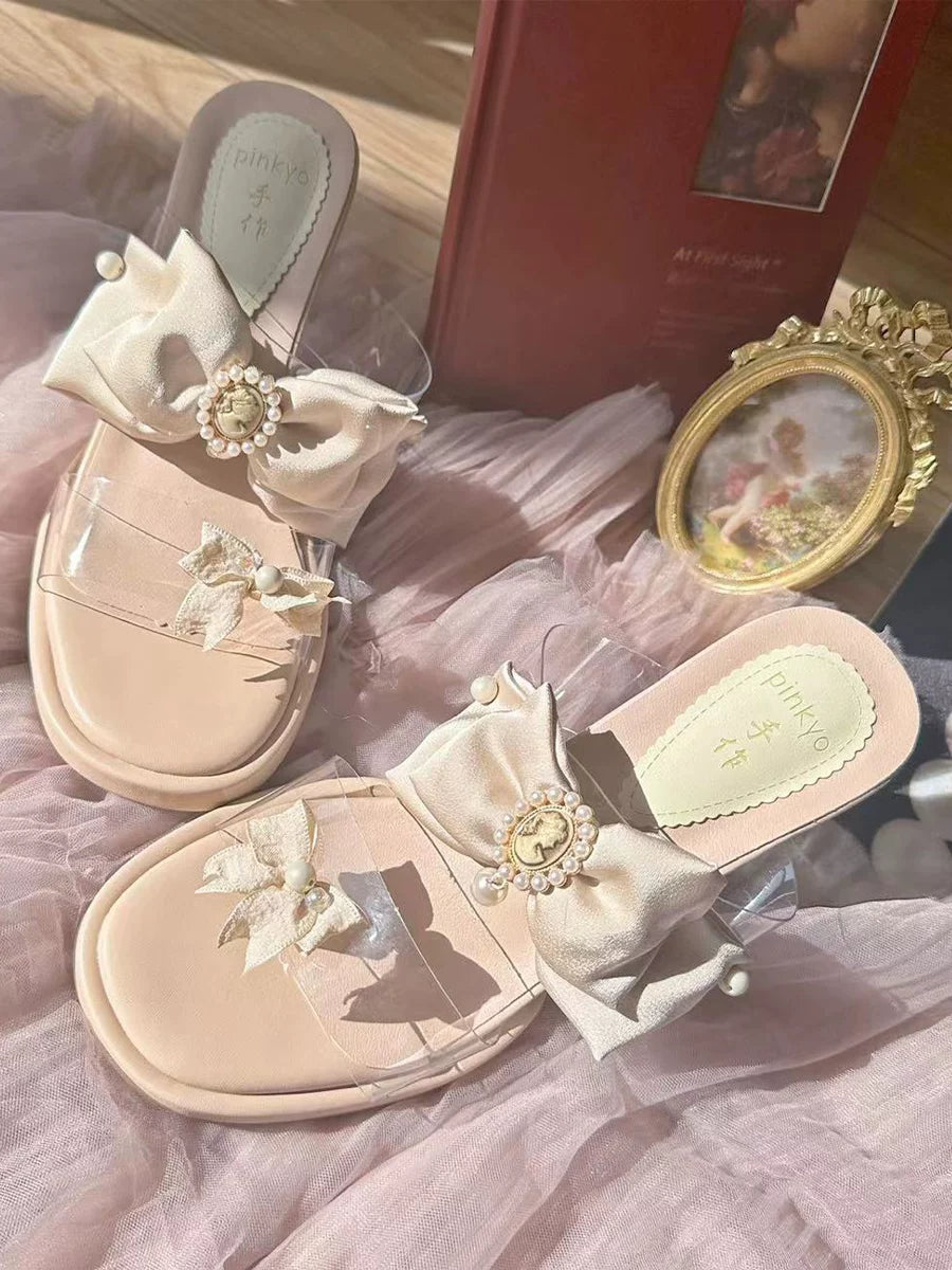 Pair of decorative sandals with floral embellishments on a soft pink fabric background.