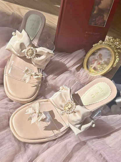 Pair of decorative sandals with floral embellishments on a soft pink fabric background.