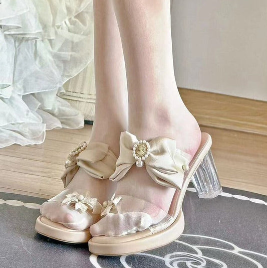 White sandals with floral details worn with sheer white stockings on a decorative floor.