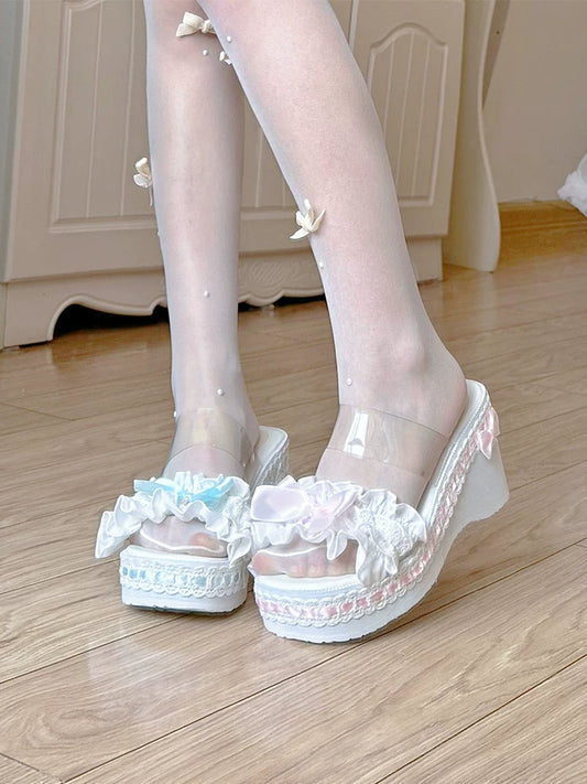 Transparent high-heeled shoes with white lace details worn by a person on a wooden floor.