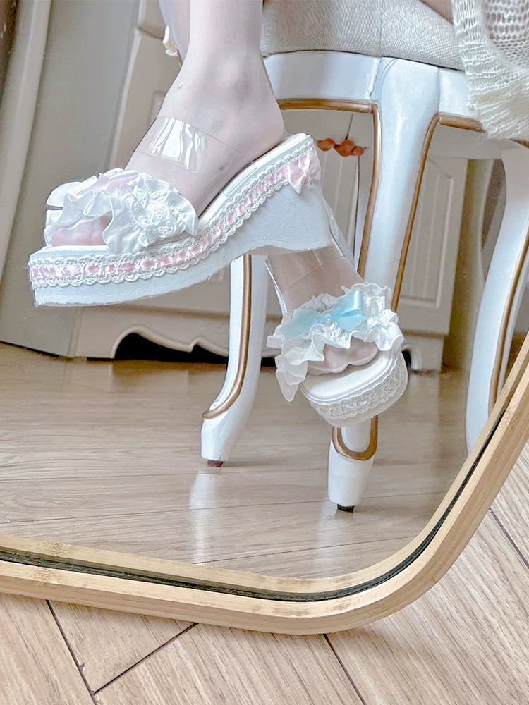 White high-heeled shoes with lace details worn by a person sitting on a chair.