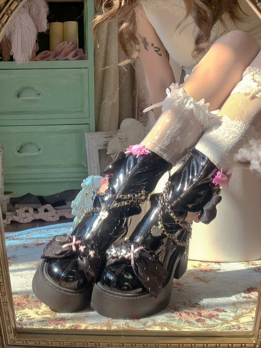 Person wearing black patent leather boots with decorative chains in front of a mirror.