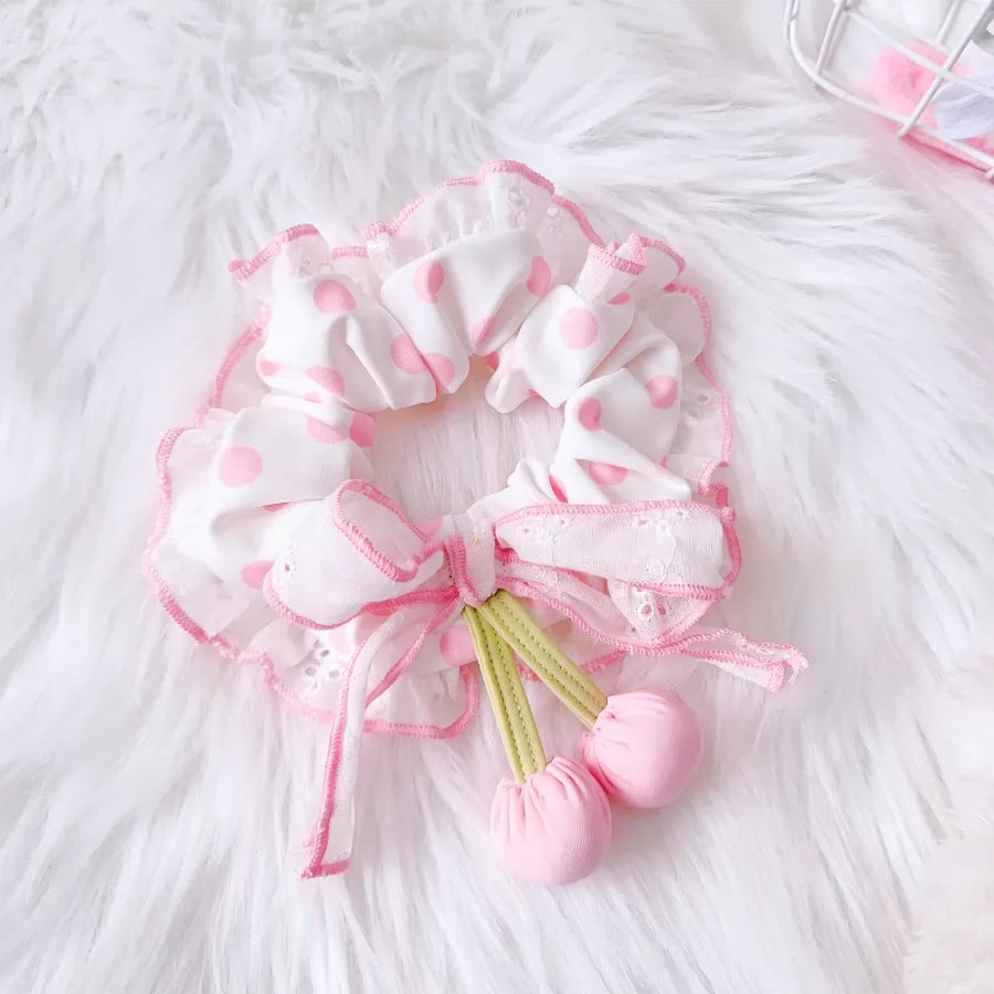 Pink scrunchie with pom-poms on a white fluffy surface
