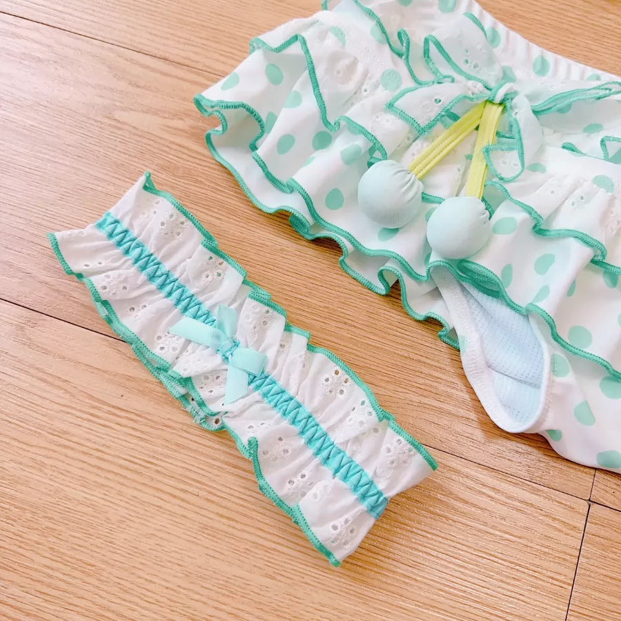 Pair of white and green polka dot baby bloomers on a wooden surface
