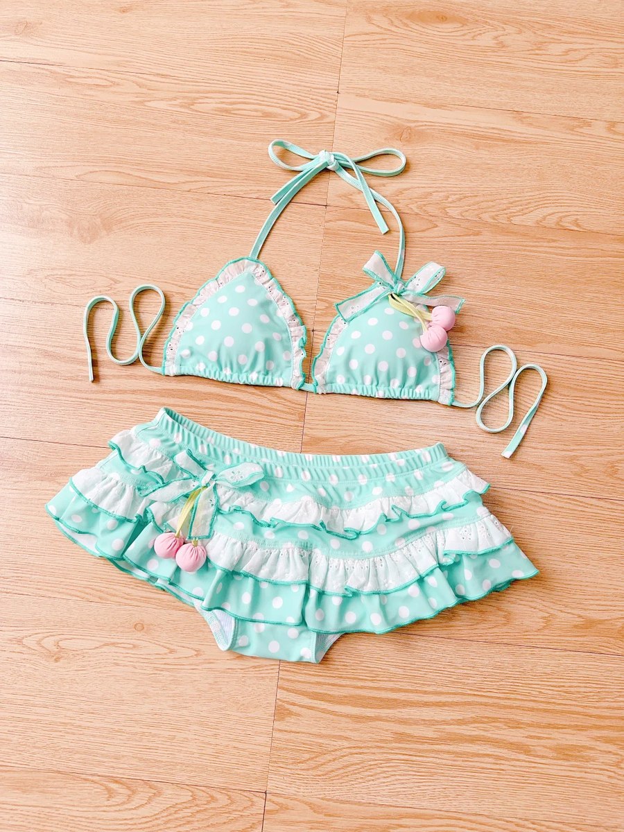 Two-piece mint green polka dot swimsuit with ruffles on a wooden floor.