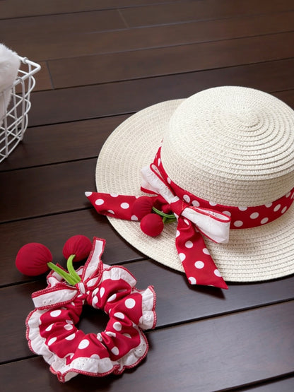 White straw hat with red polka dot ribbon and matching red polka dot scrunchie on a wooden surface