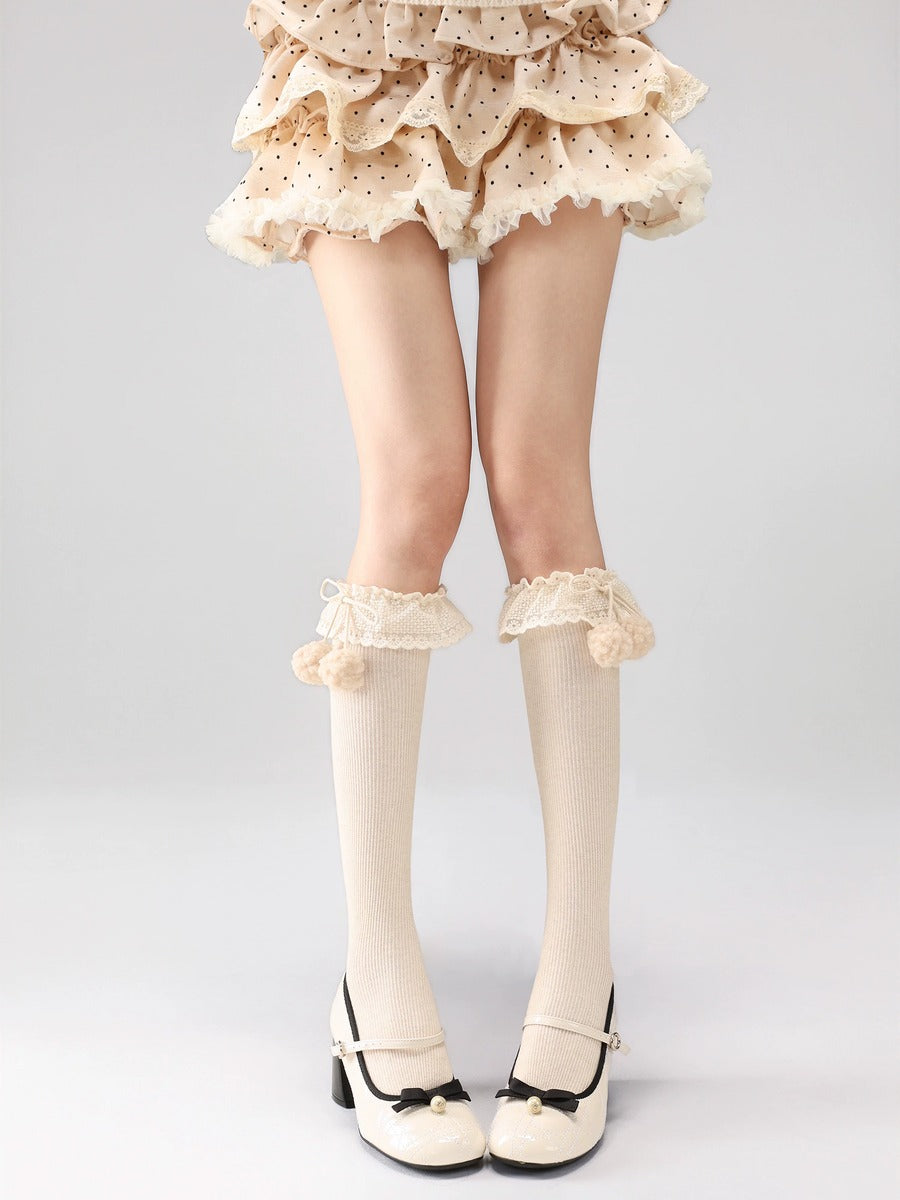 Legs wearing white knee-high socks with ruffles and a polka dot skirt on a gray background