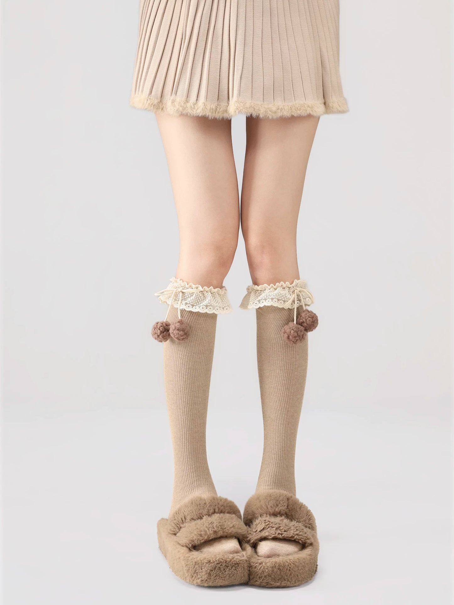 Person wearing beige knee-high socks with lace details and fluffy slippers on a light gray background