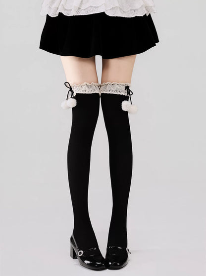 Black thigh-high stockings with white pom-poms and lace trim worn with a black skirt and shoes on a light gray background.