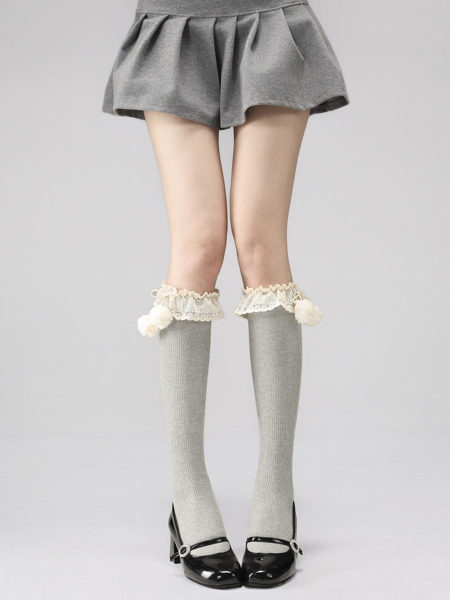 Person wearing a gray skirt, gray knee-high socks with white lace trim, and black shoes on a light gray background.