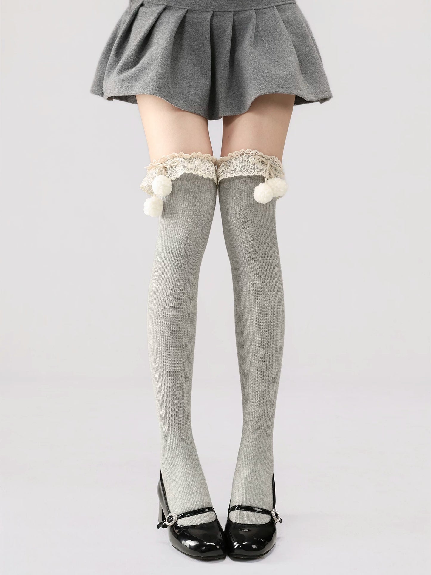 Gray knee-high socks with lace and pom-poms worn with a gray skirt on a white background