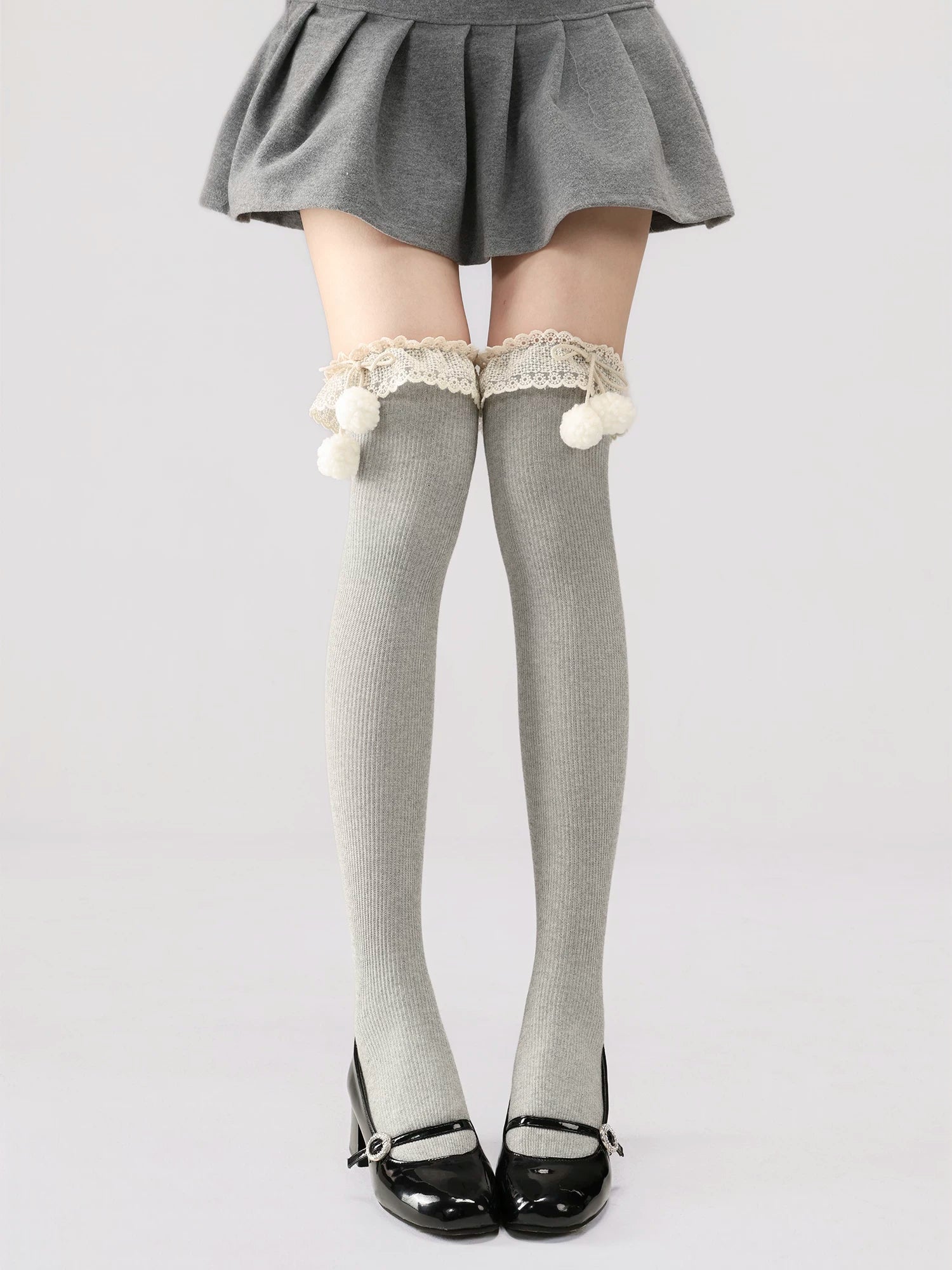 Gray knee-high socks with lace and pom-poms worn with a gray skirt on a white background