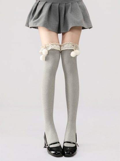 Gray knee-high socks with lace and pom-poms worn with a gray skirt on a white background
