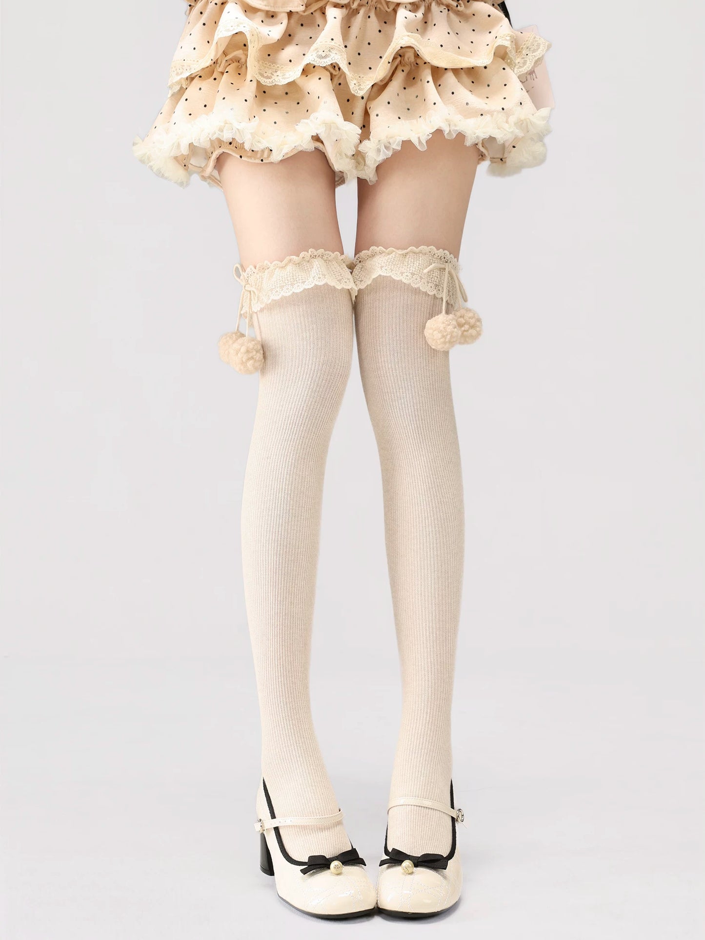 White tights with lace details and pom-poms worn by a person on a light gray background