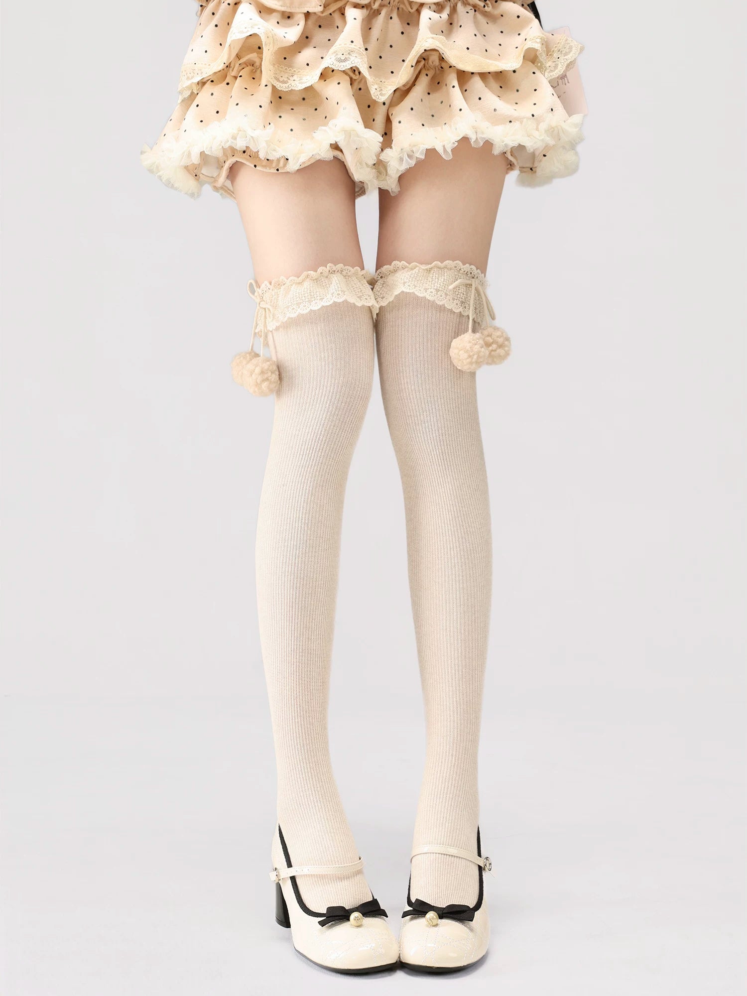 White tights with lace details and pom-poms worn by a person on a light gray background