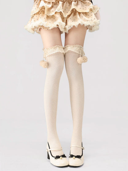 White tights with lace details and pom-poms worn by a person on a light gray background